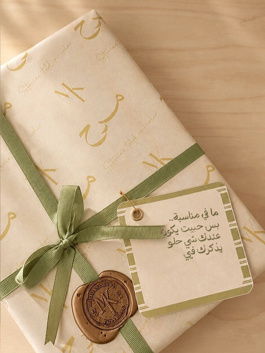 Cream gift wrap with gold calligraphy patterns, green ribbon, and a wax seal.