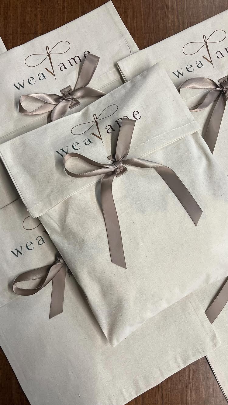 Cream fabric gift bags tied with satin bows on a wooden table.