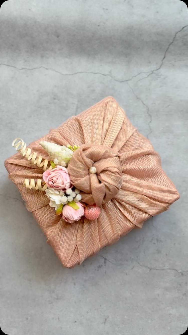 Peach fabric wrapped gift with a central knot and small pink floral decorations.