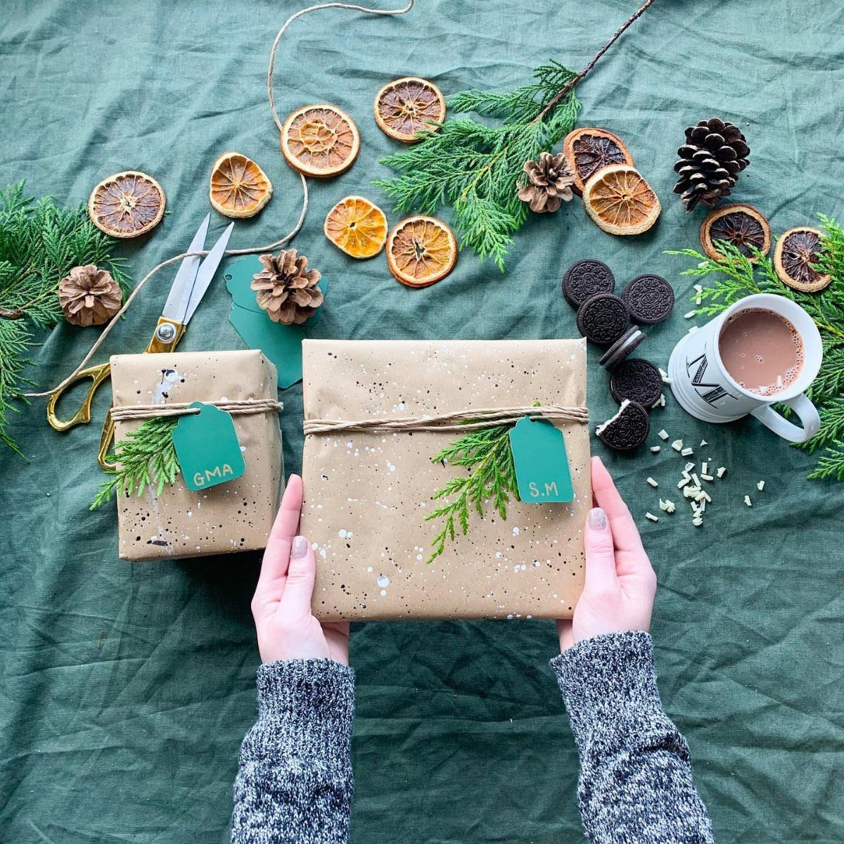 Splatter paint wrapped brown paper gifts with dried orange slices and pine cones.