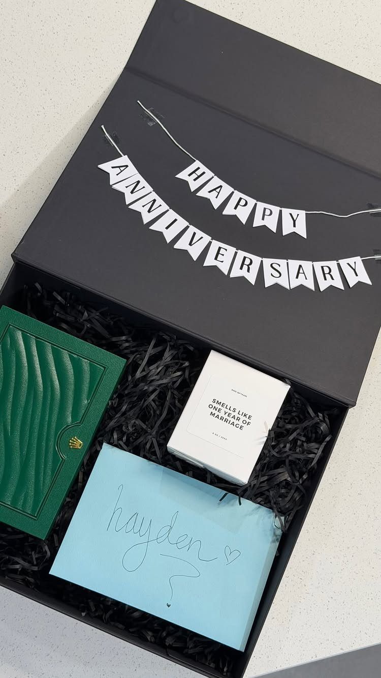 Black anniversary gift box containing a green notebook, white candle, and blue envelope.