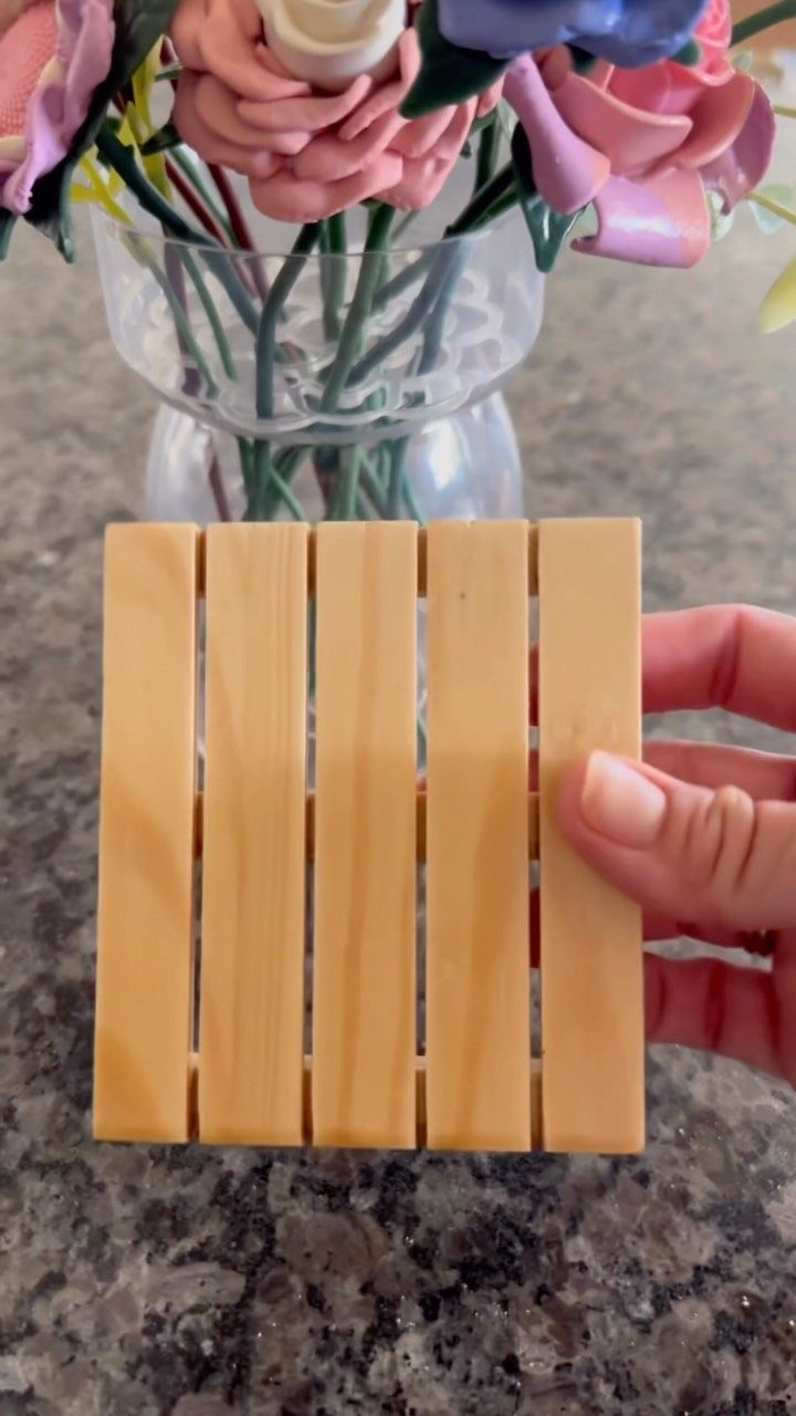 Miniature wooden pallet coaster held by a hand against a floral background.