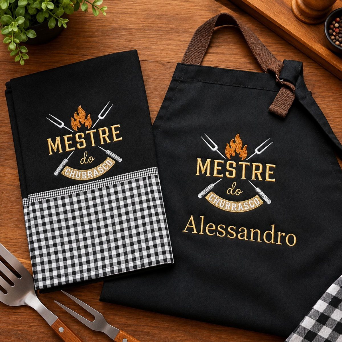 Black personalized grilling apron and matching towel with gold text on wooden table
