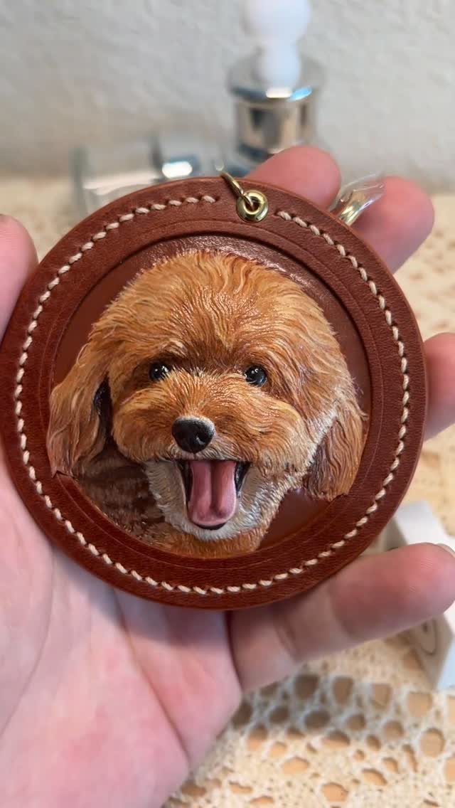 Hand holding a leather keychain with a realistic painting of a brown dog
