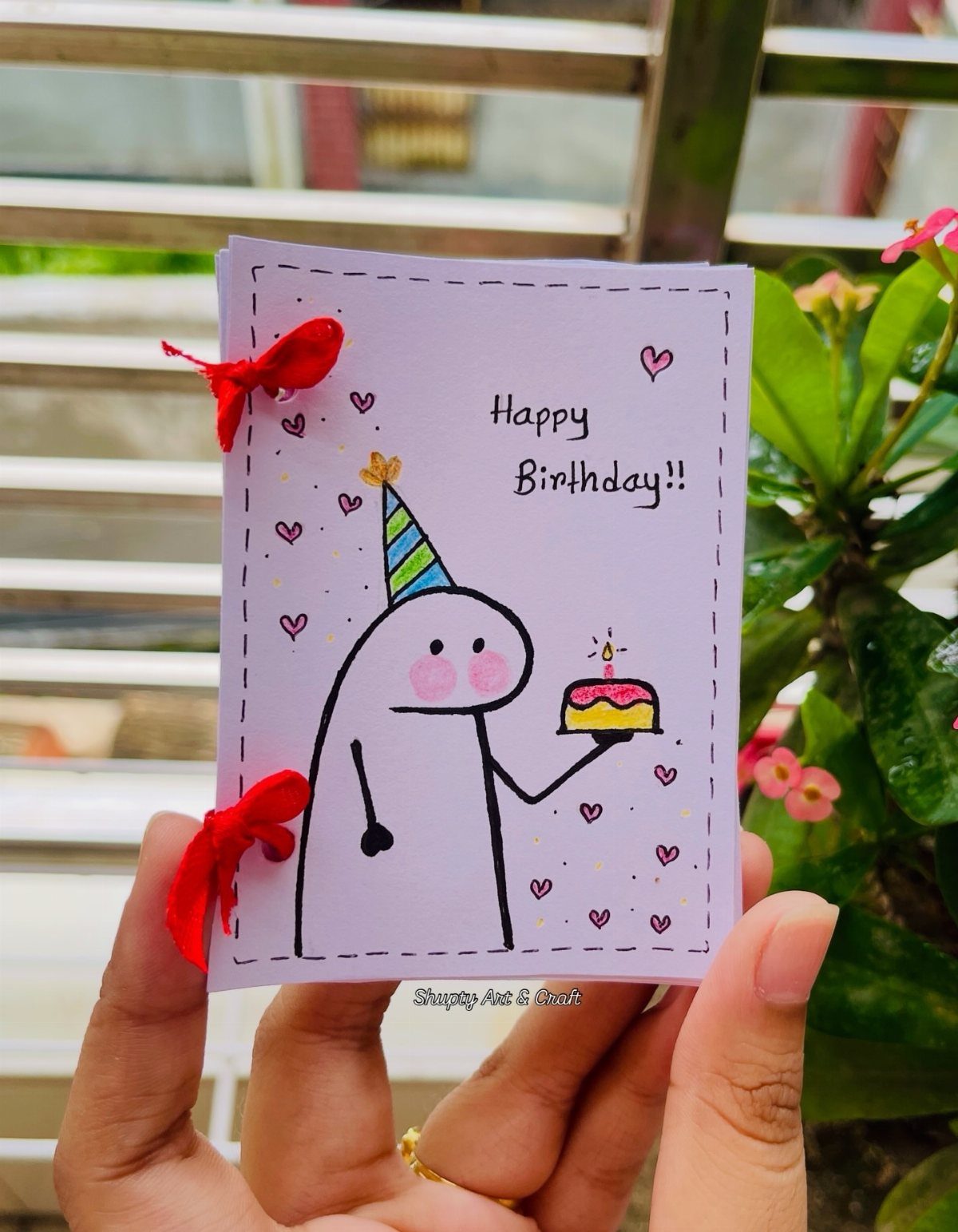 Handmade purple birthday card with a cute character holding a cake and red ribbons.