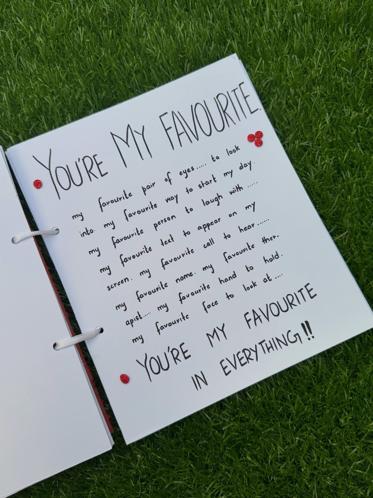 Handmade notebook page with handwritten love notes and red gems on green grass