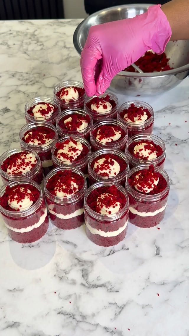 Red velvet cake jars with white frosting being prepared on marble surface