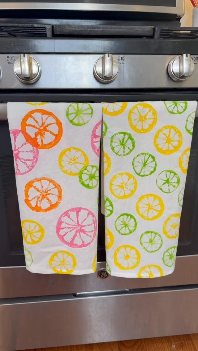 White kitchen towels with colorful stamped citrus slices hanging on an oven handle.