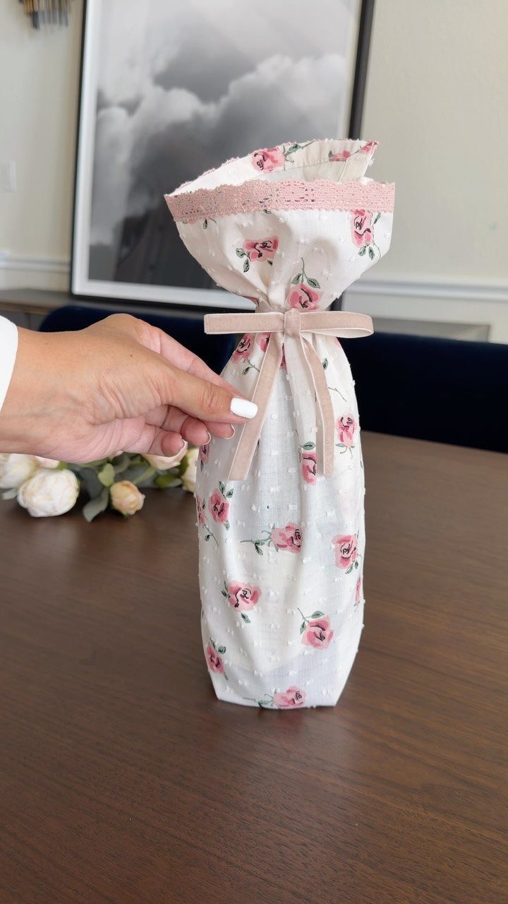 Bottle wrapped in floral fabric with a pink ribbon bow on a table