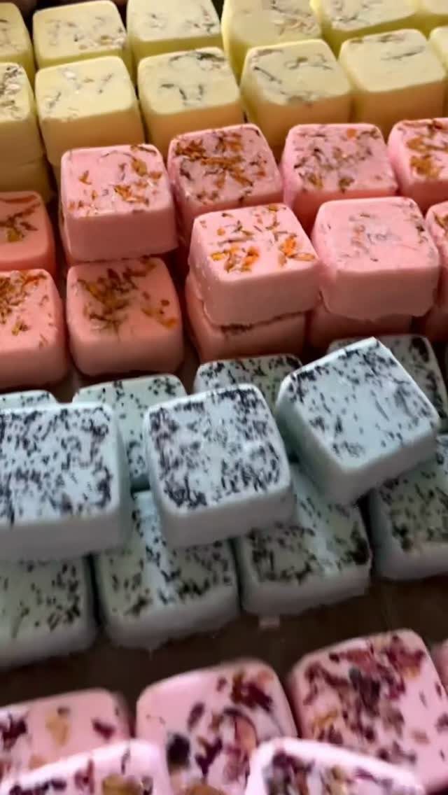 Square bath bombs in yellow, pink, and blue with dried botanical inclusions.