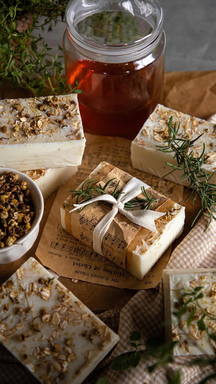 Handmade white soap bars topped with oats and herbs, one wrapped with ribbon.