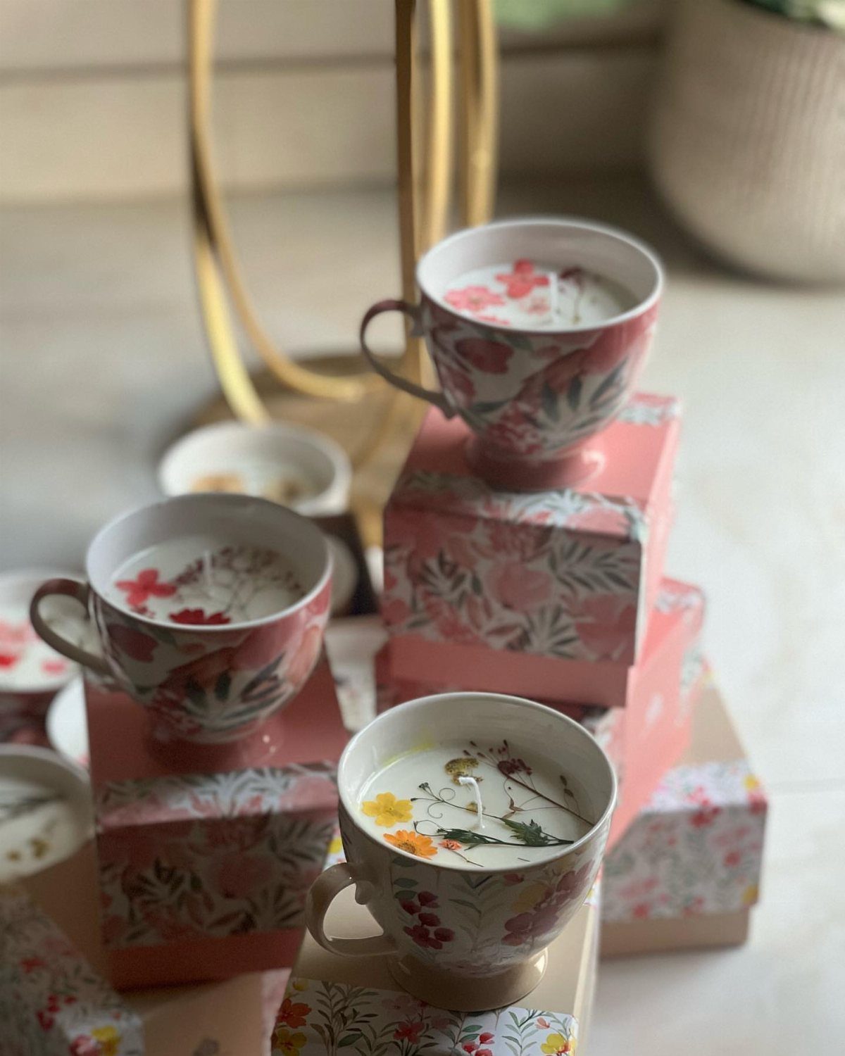 Floral teacups filled with white candles resting on pink floral gift boxes.