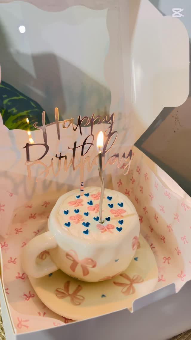 Teacup shaped birthday cake with blue hearts and a lit candle in a box