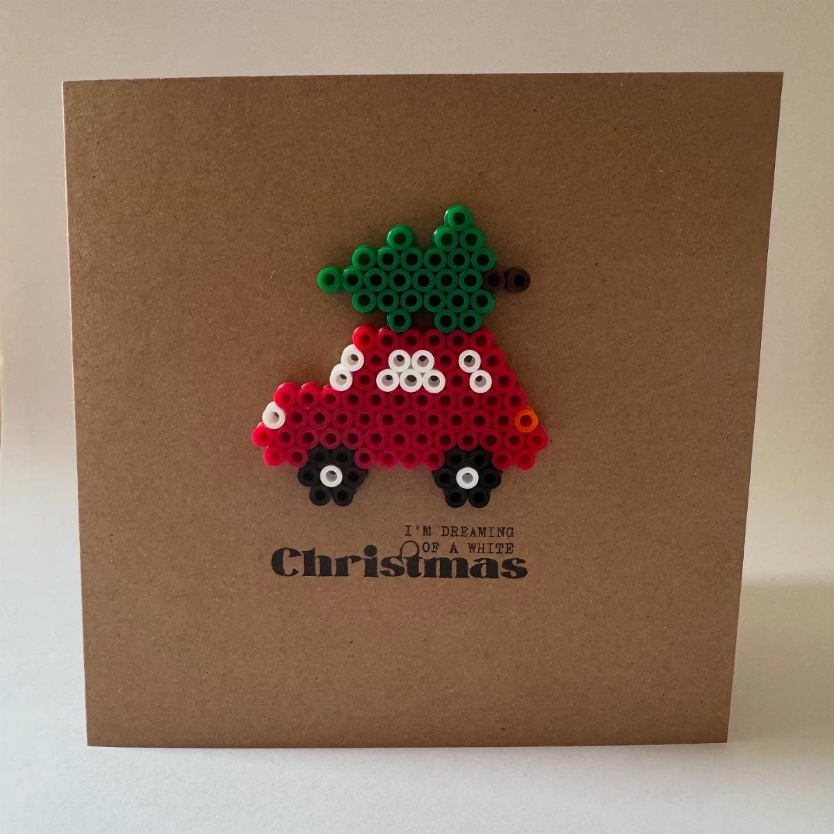 Brown greeting card with a red car and green tree made of beads.