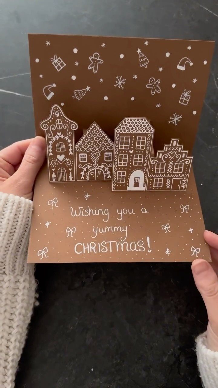 Brown Christmas card with pop-up gingerbread houses and white hand-drawn festive doodles.
