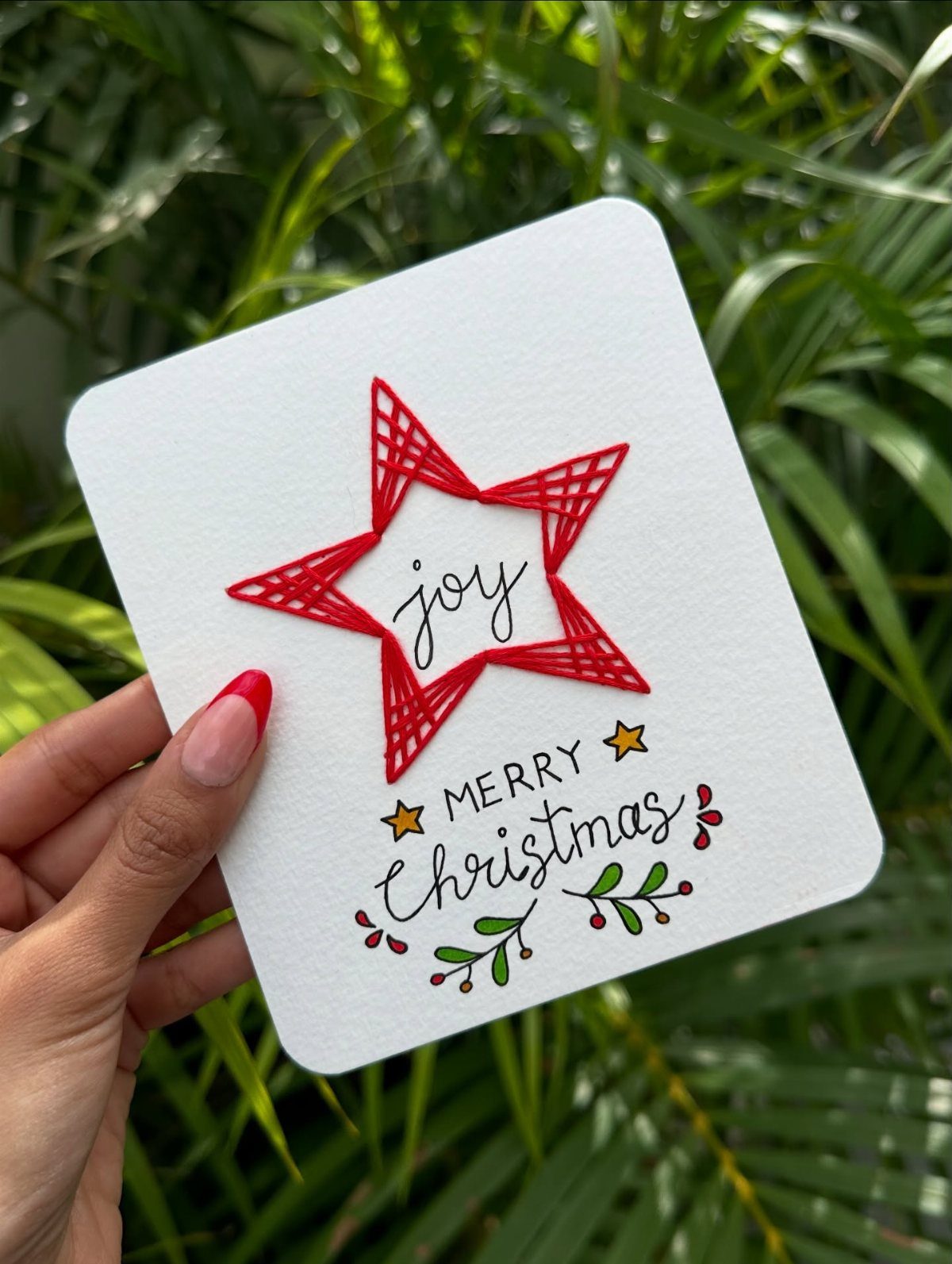 White Christmas card with a red string art star and festive lettering.