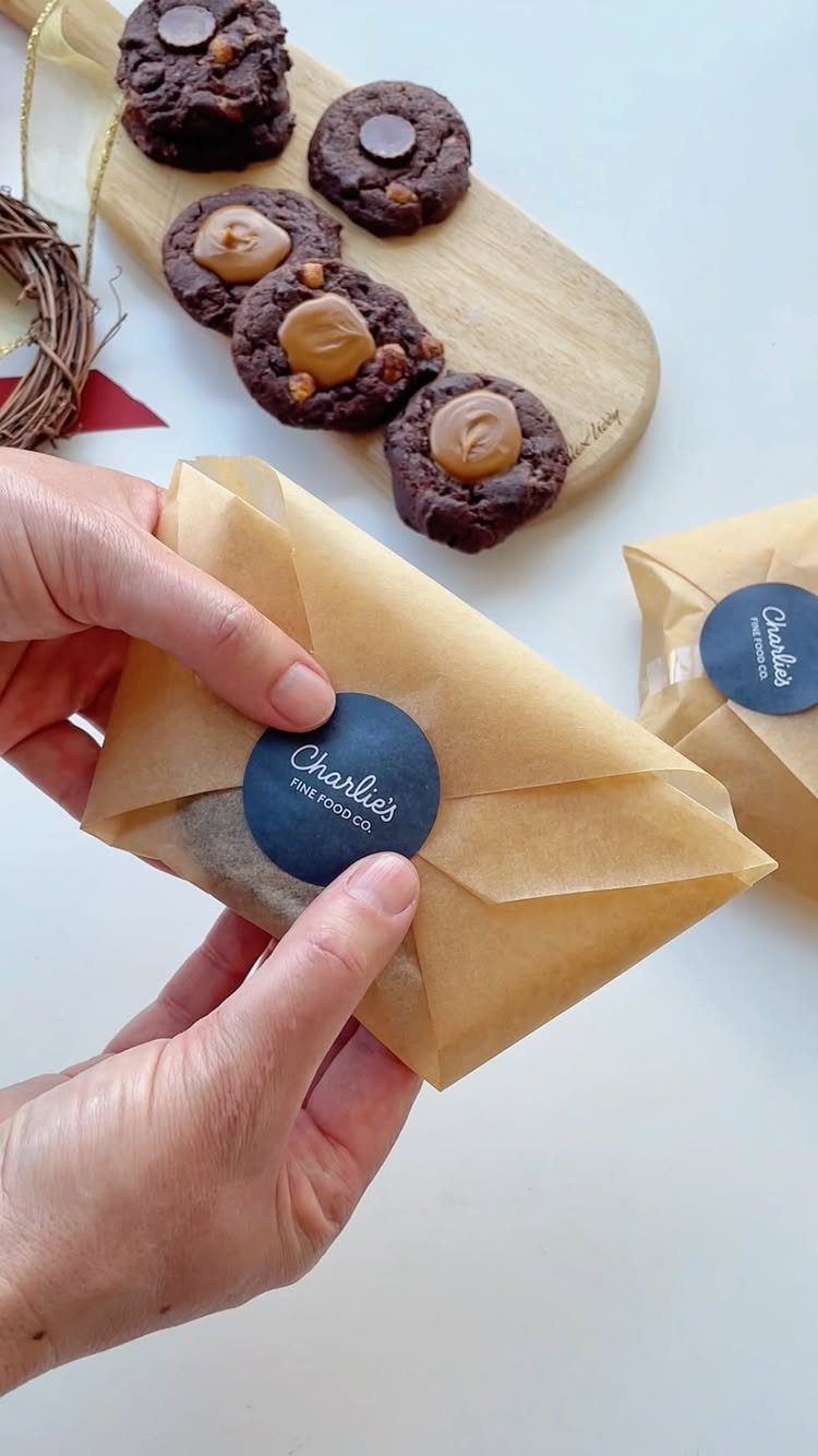 Hands sealing a brown paper bag of cookies with a blue brand sticker.