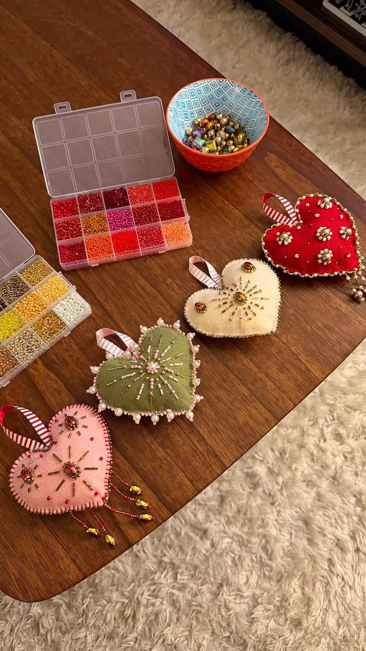 Heart-shaped fabric ornaments with beads and sequins on a wooden table with craft supplies.
