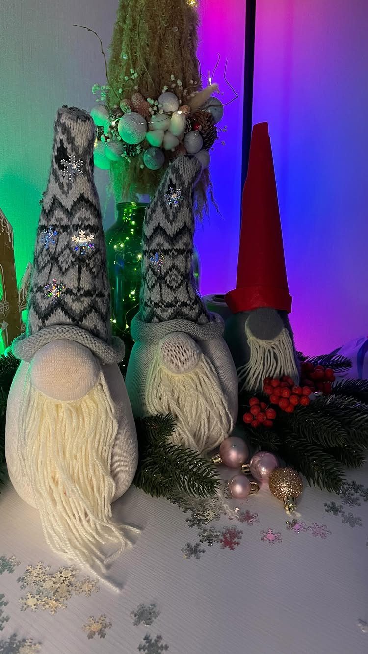Three Christmas gnomes with knit hats and long beards among holiday greenery.