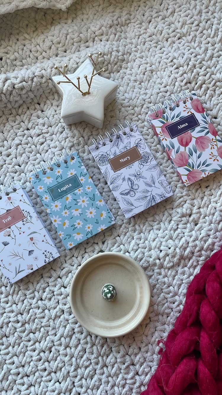 Four personalized floral spiral notebooks resting on a white chunky knit blanket.