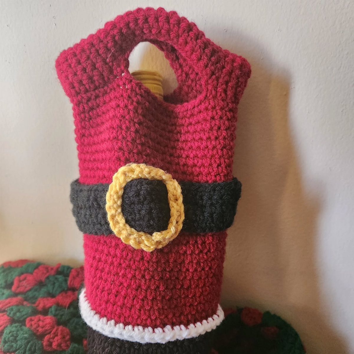 Crocheted red Santa Claus wine bottle bag with black belt and yellow buckle.