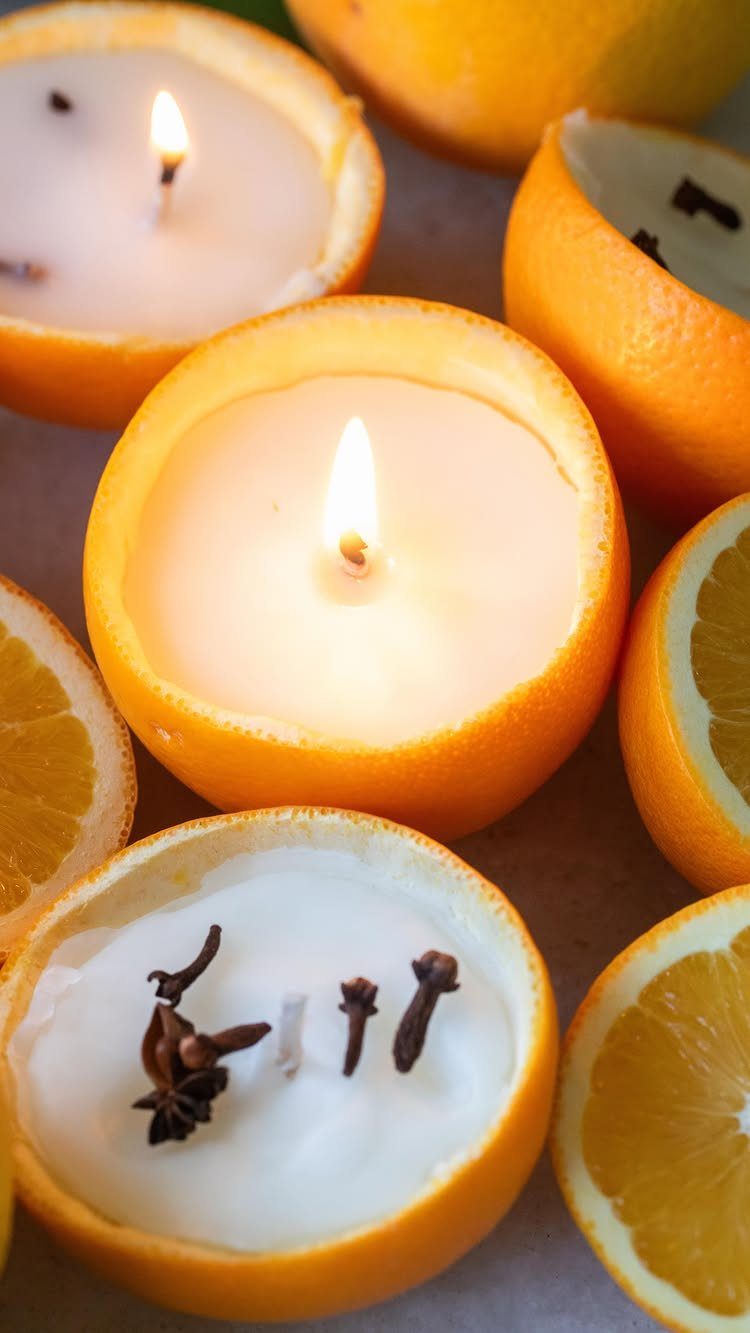 White wax candles poured into orange peel halves, some lit and decorated with cloves.