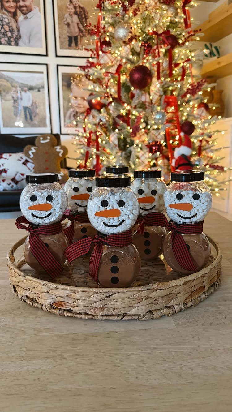 Snowman-themed jars filled with hot cocoa mix on a tray before a Christmas tree.