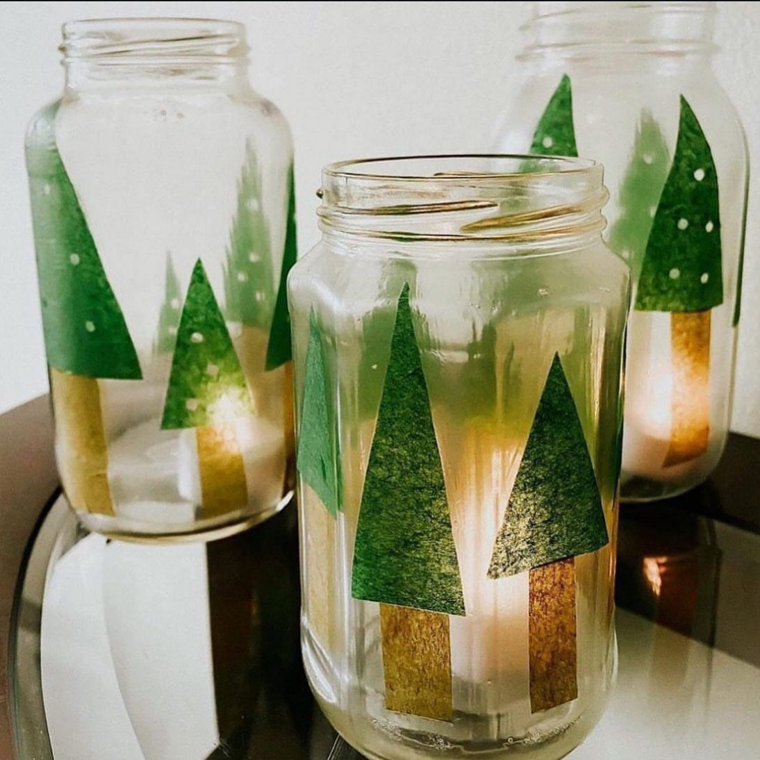 Mason jar luminaries with green paper Christmas trees and glowing tea light candles.