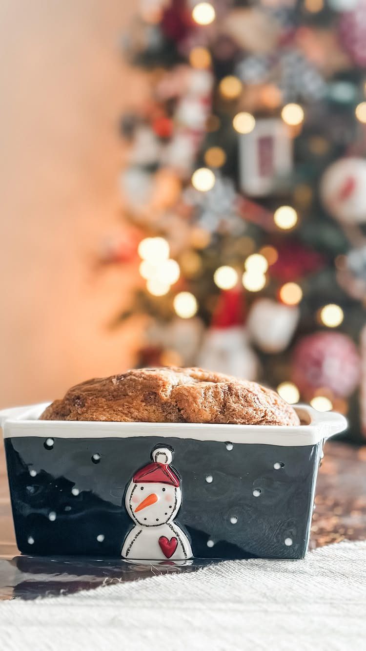 Baked bread in a black snowman ceramic dish with a blurred Christmas tree background