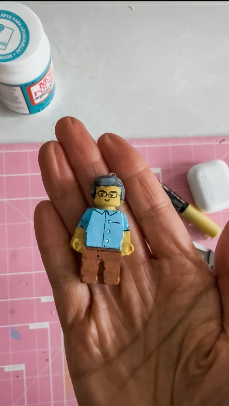 Hand-painted LEGO minifigure held in a palm on a pink craft mat.