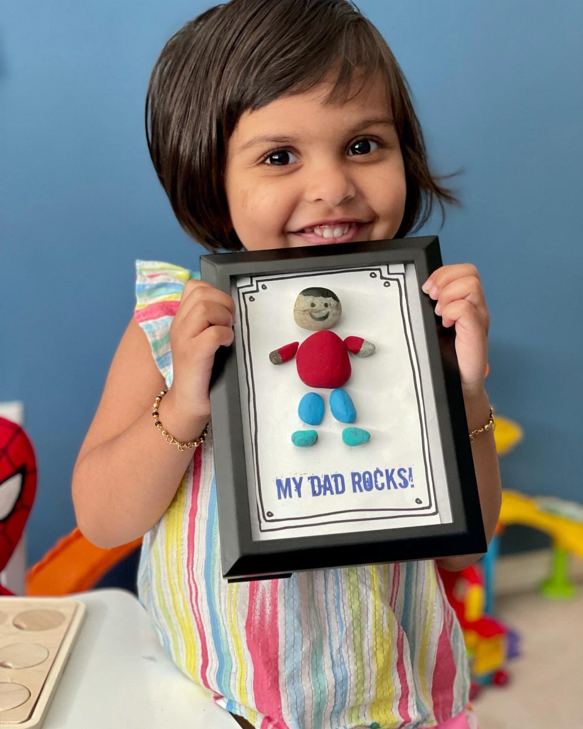 Young girl holding a framed rock art figure that says My Dad Rocks!