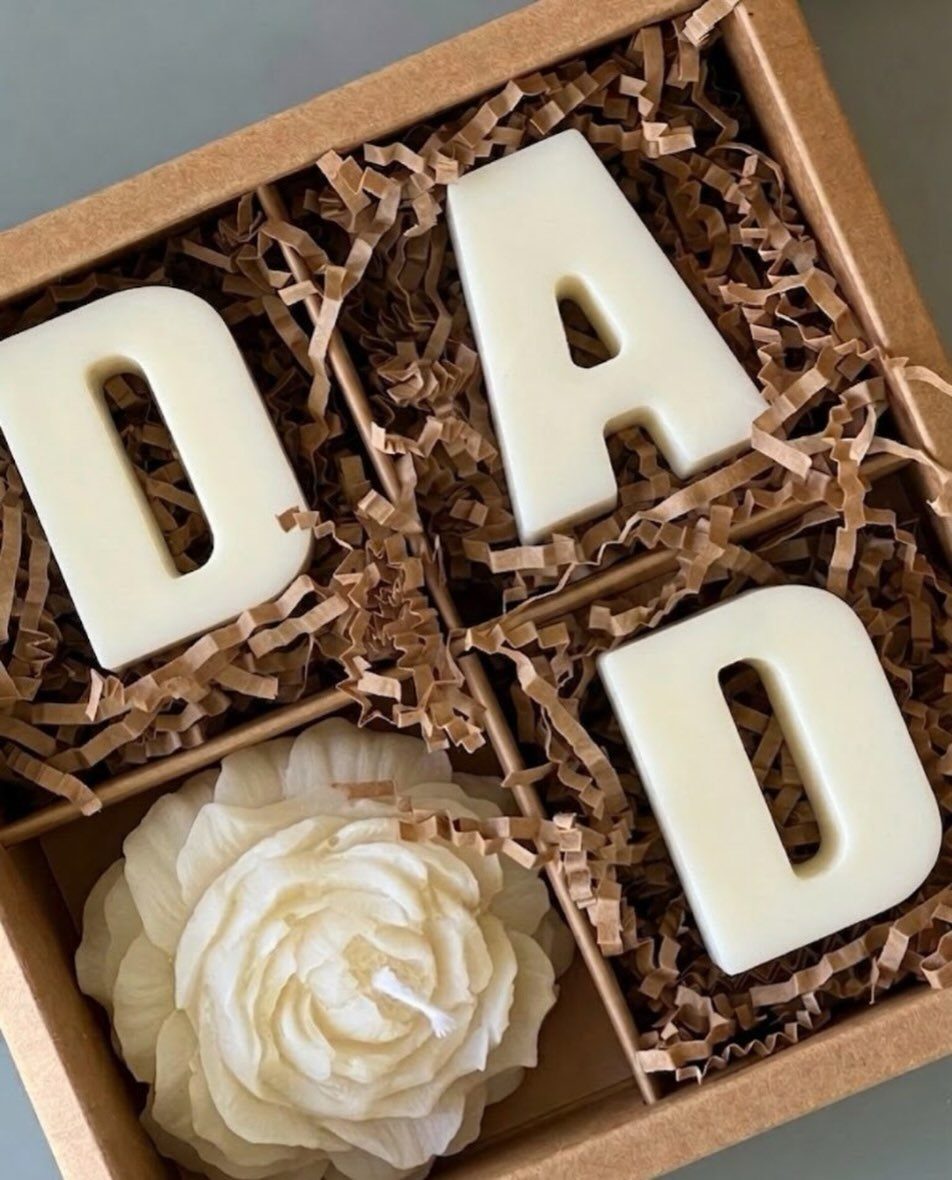 White wax candles shaped as the word DAD and a flower in a box.