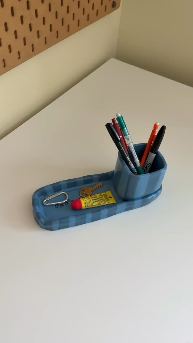 Blue striped clay dish and pen holder containing keys and colorful pens.
