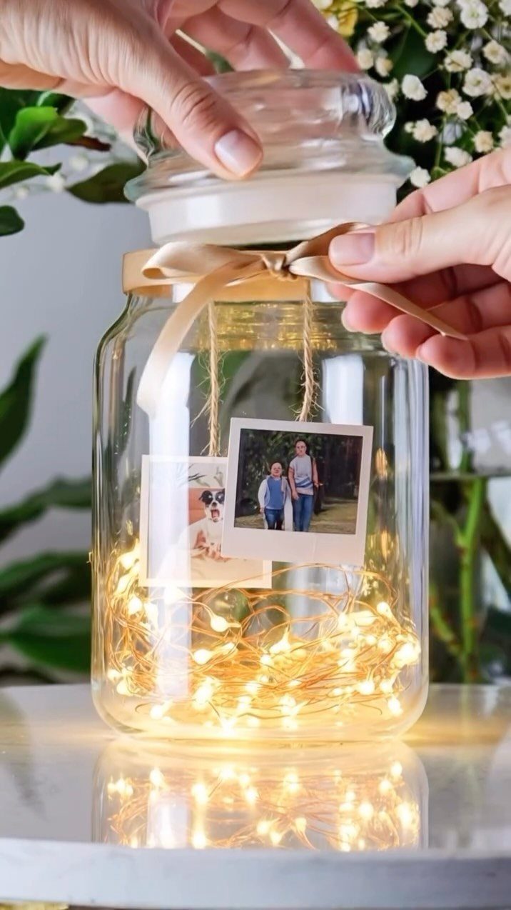 Glass jar with fairy lights, a candle, and hanging photos tied with ribbon.