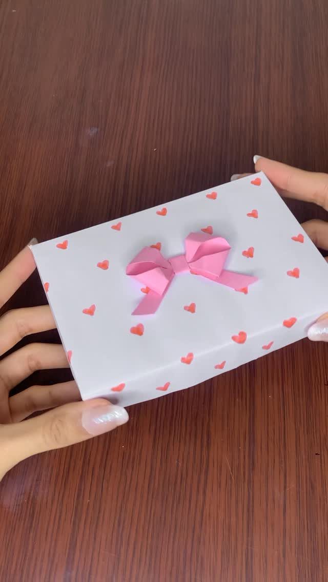 White gift box with red hearts and a pink bow held by hands.