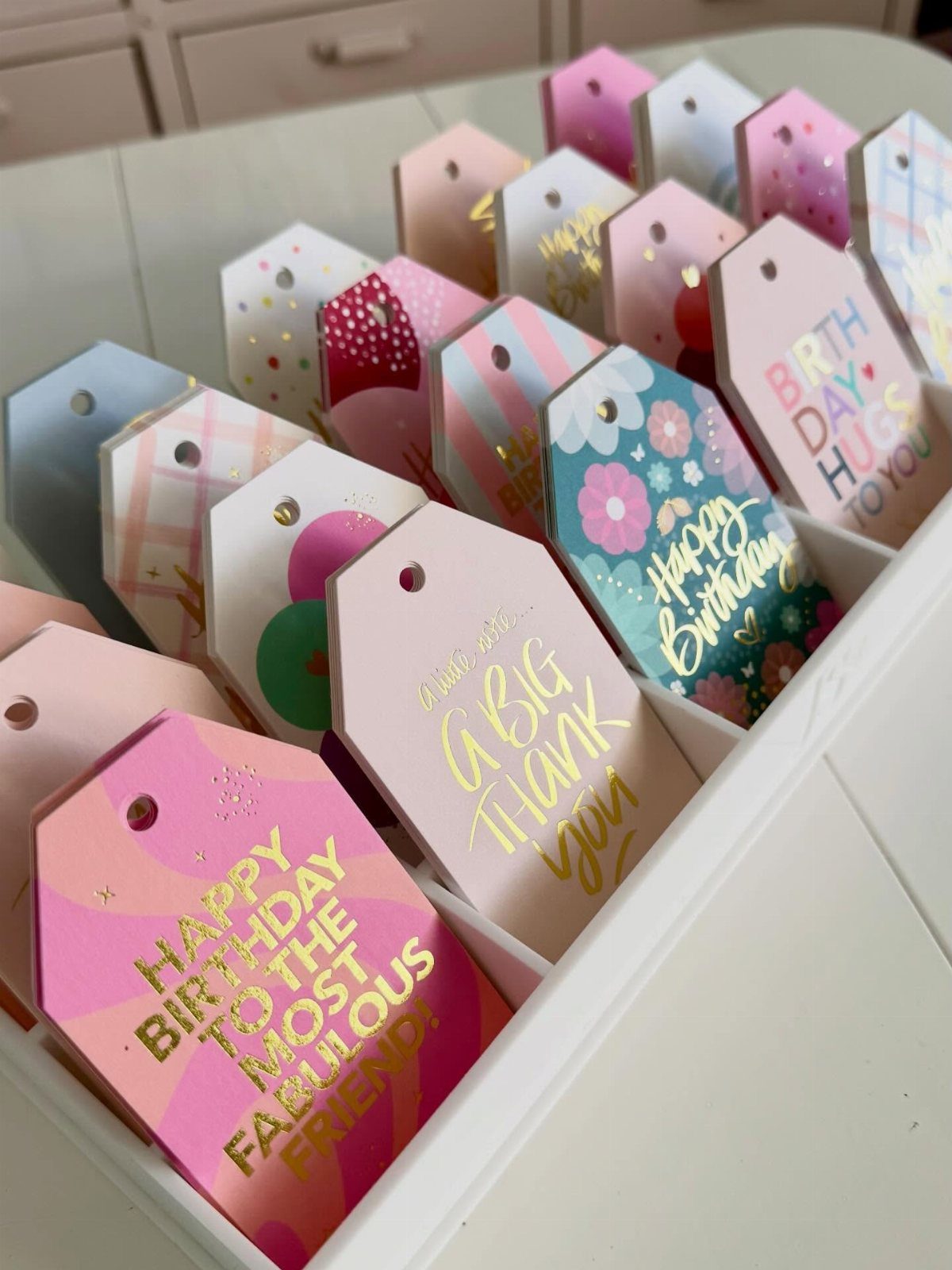 Colorful printed gift tags with bold lettering arranged in a white organizer tray.