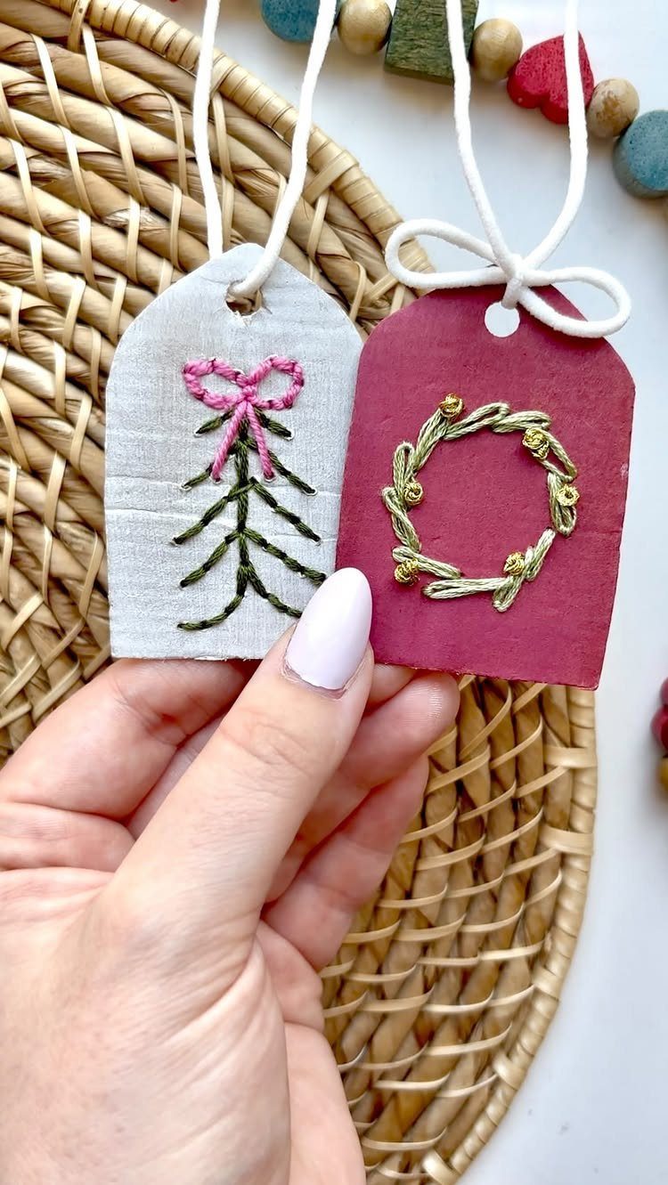 Two embroidered gift tags, one grey and one red, held over a straw mat.
