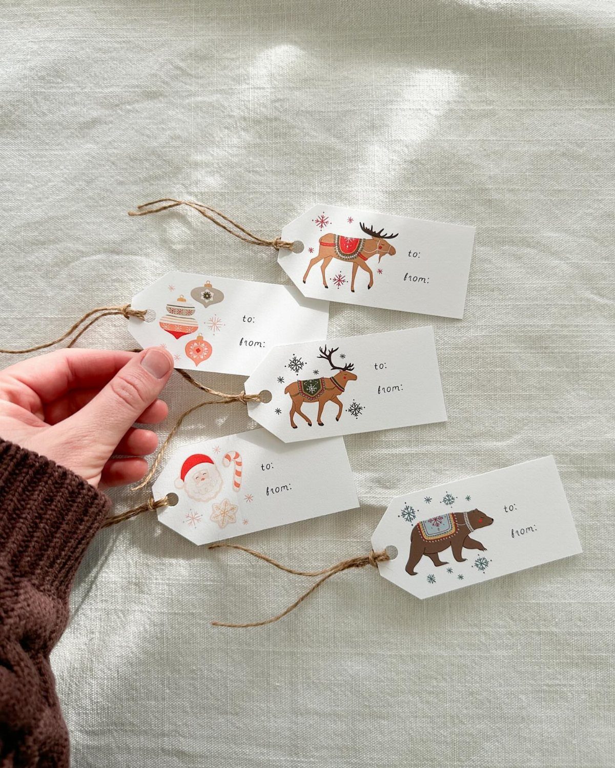 White printed gift tags with winter animals and ornaments held by a hand.