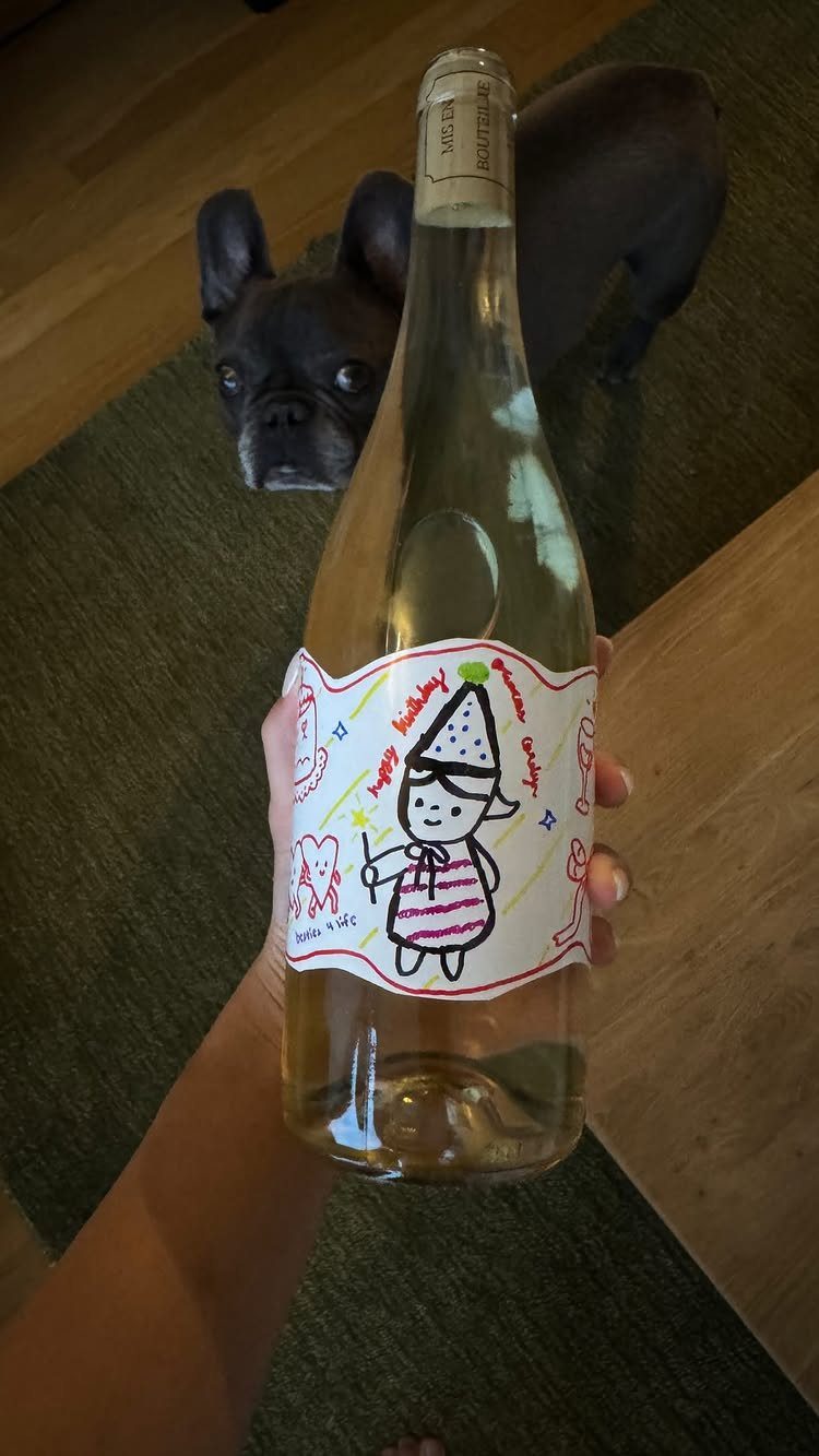 Wine bottle with a handmade birthday drawing label held in front of a dog