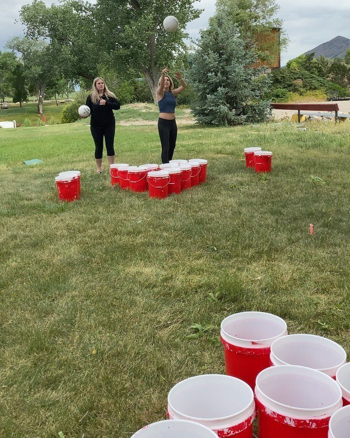 Two women playing giant beer pong with red buckets on a grassy lawn