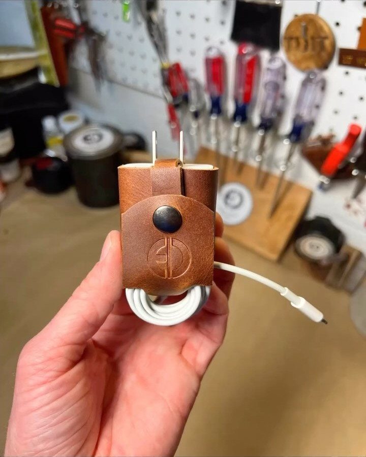 Brown leather cord keeper holding a white charging cable in a workshop setting