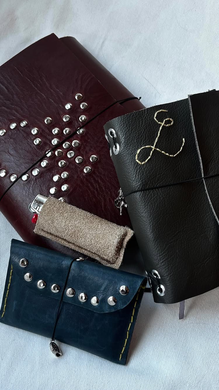 Three handmade leather journals in burgundy, black, and navy blue on white fabric.