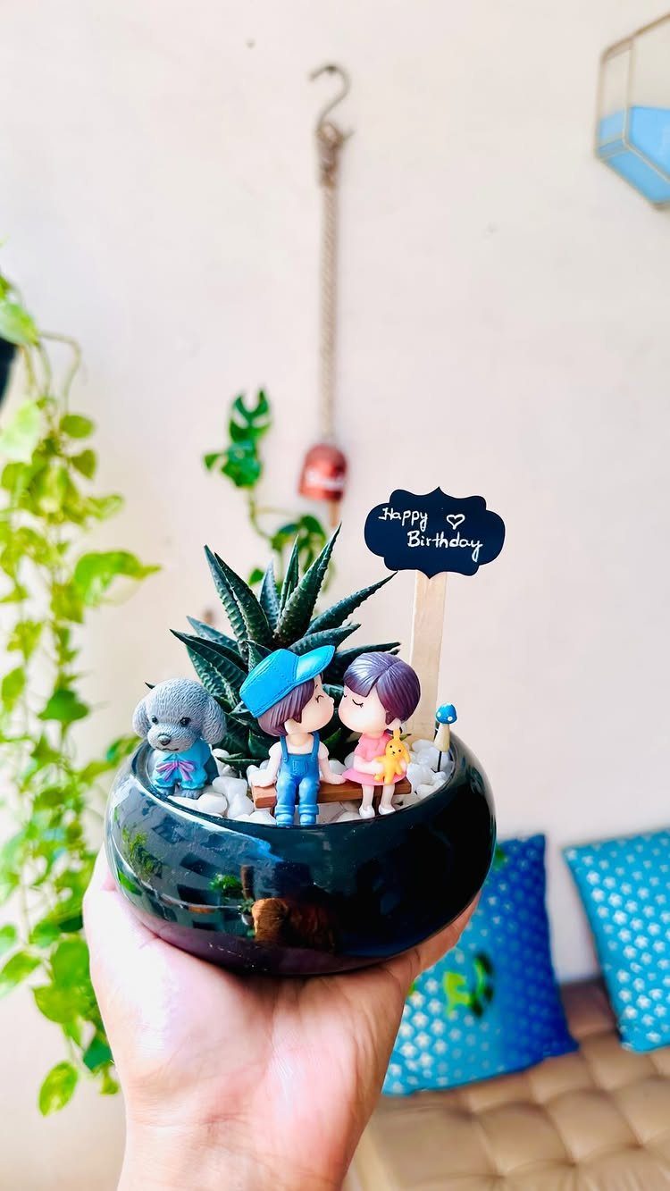 Small black succulent planter with couple figurines, a dog, and birthday sign.