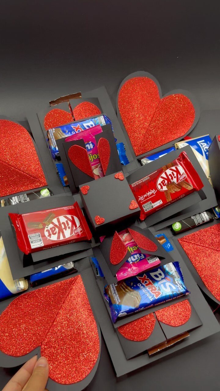 Black explosion gift box filled with chocolates and red glittery hearts on a dark background