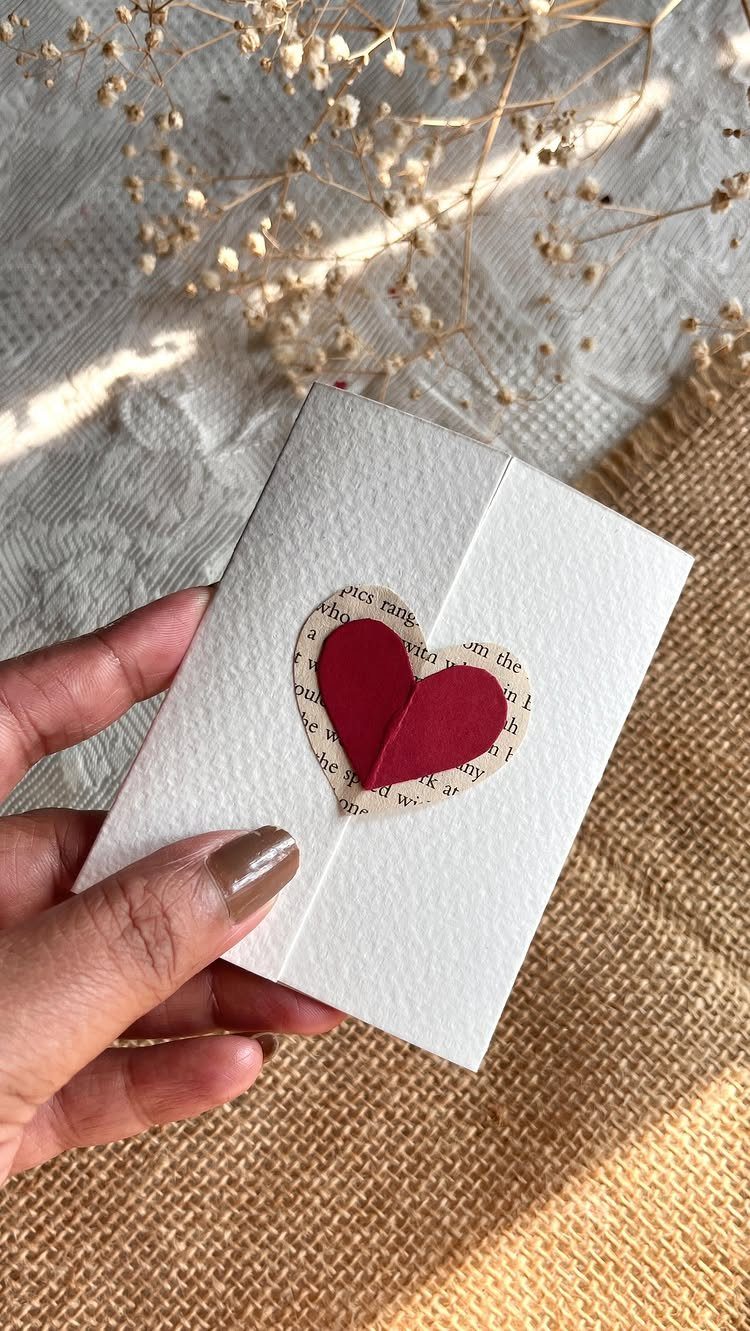 Hand holding a white envelope decorated with a red paper heart and text.