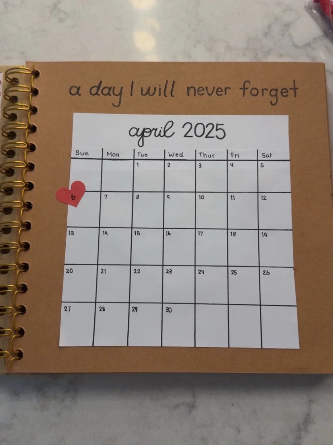 Brown spiral notebook showing a calendar page with a red heart on April 6th