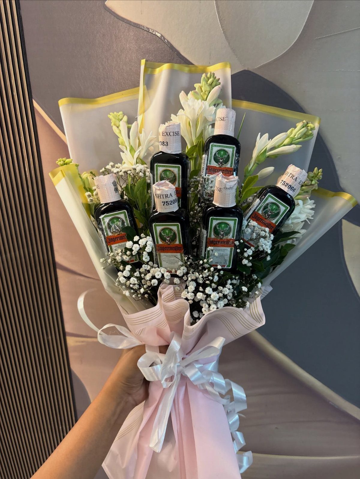 Bouquet of white flowers and small liquor bottles wrapped in pink paper.