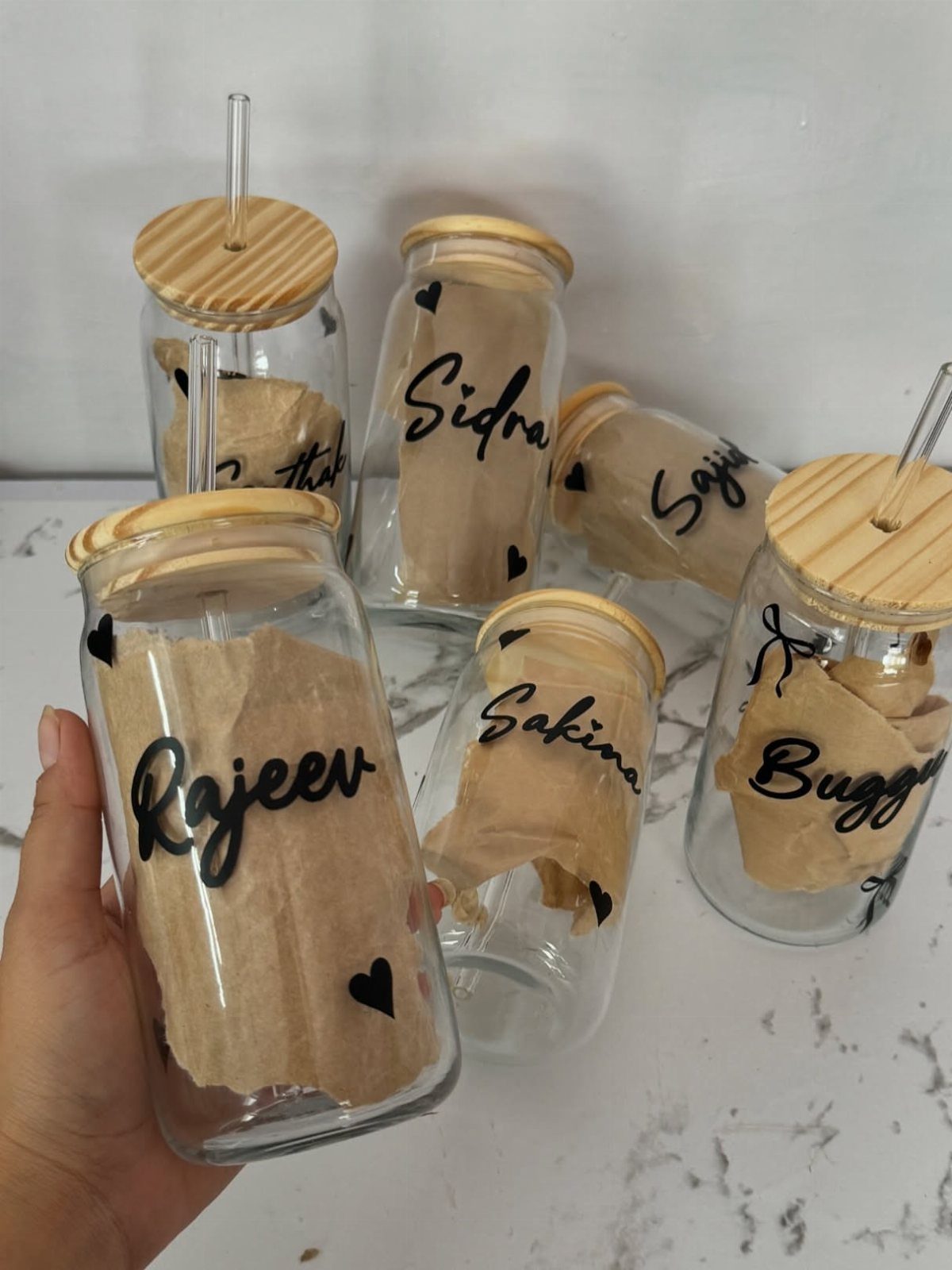 Glass jars with bamboo lids containing personalized notes and names written in cursive.