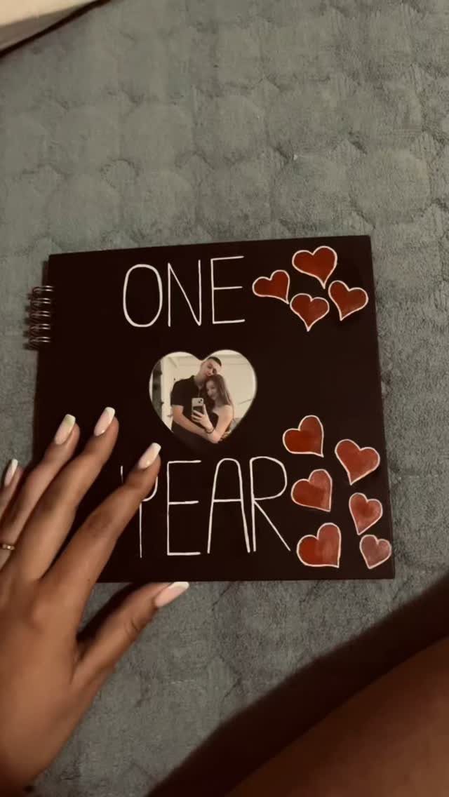 Black spiral scrapbook cover with 'ONE YEAR' text, red hearts, and couple photo.