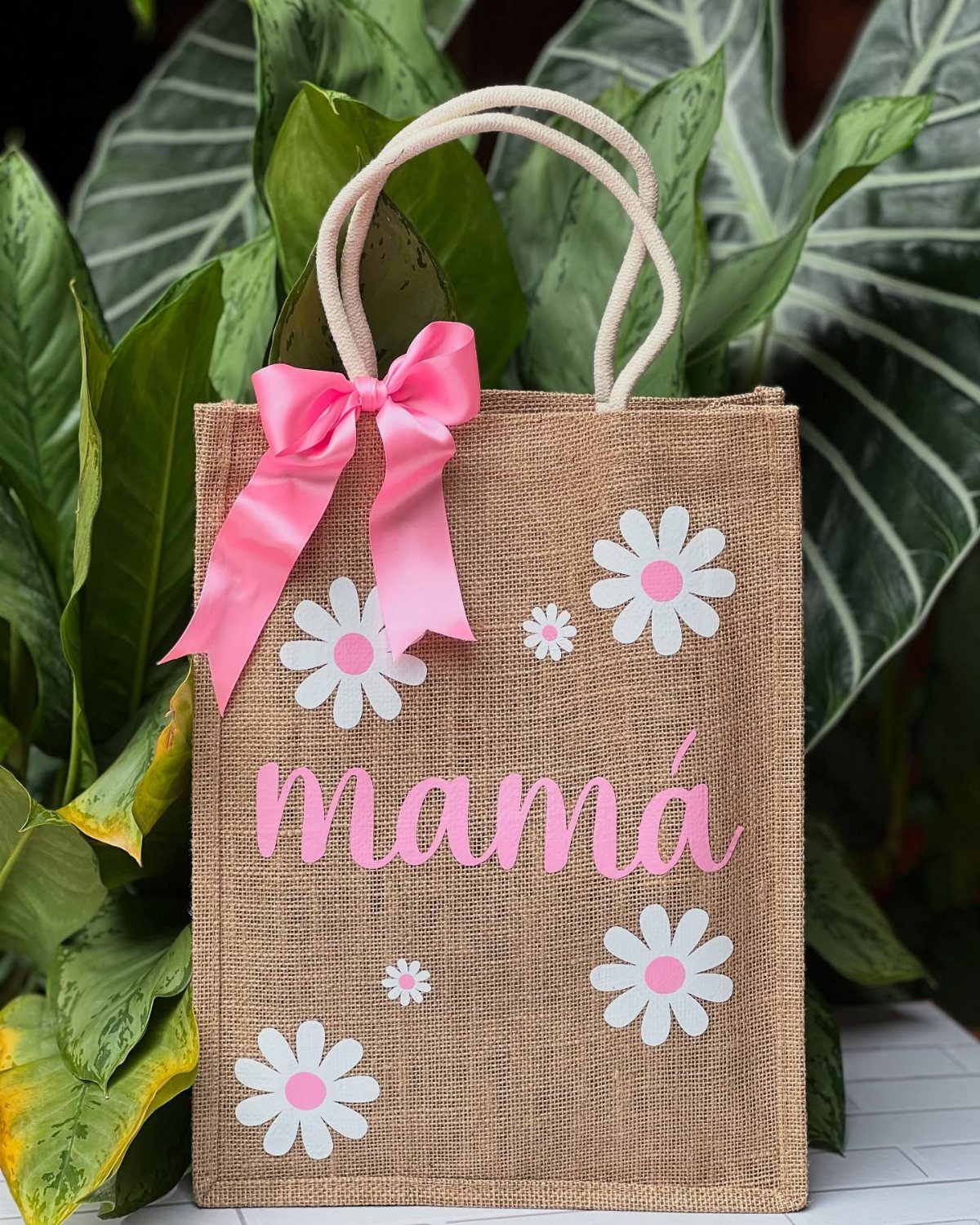Burlap tote bag decorated with pink daisies and the word mamá in pink.